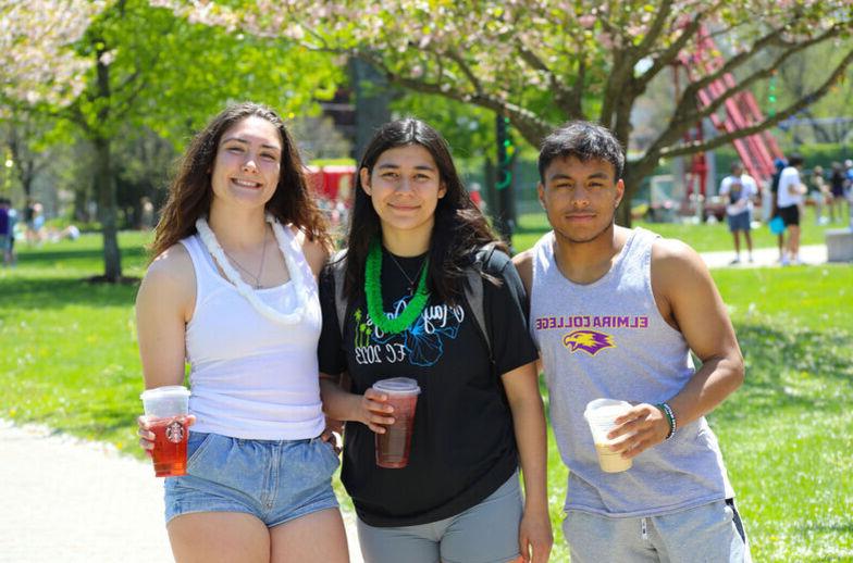 A male student and two female students hold cold drinks while smiling for the camera outside during May Days